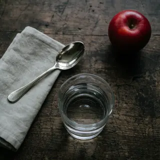 A still life on a wooden table featuring a clear glass of wa