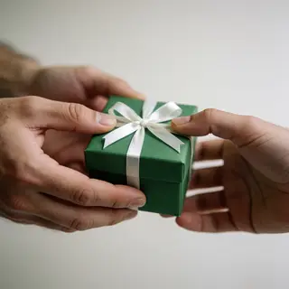 One person handing a small gift box to another person, both 