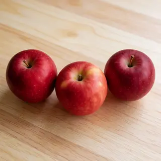 Exactly 3 red apples arranged on a wooden table