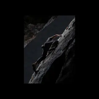 A rock climber clinging to a cliff face with arms and legs e