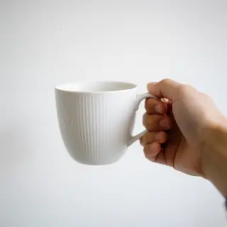 A person holding a white ceramic coffee mug by the handle wi
