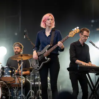 Three musicians on stage: a tall woman with short pink hair 