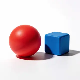 A red ball and a blue cube sitting side by side on a white s