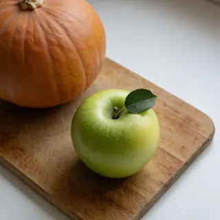 A green apple and an orange pumpkin on a wooden cutting boar
