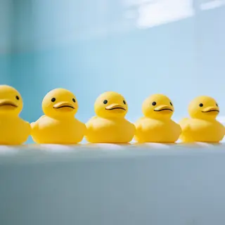 Exactly 5 yellow rubber ducks sitting in a row on a bathroom