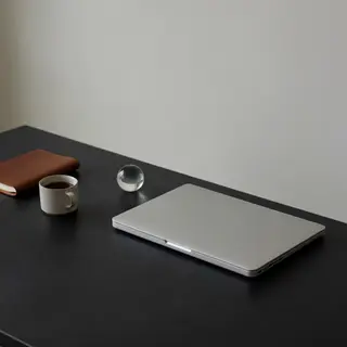 A workspace desk with a brushed aluminum laptop, a leather-b