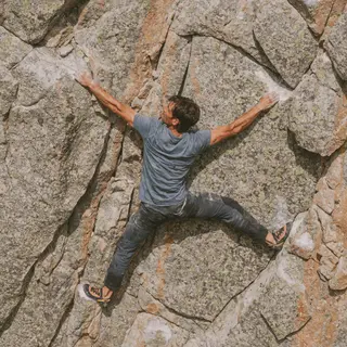 A rock climber clinging to a cliff face with arms and legs e