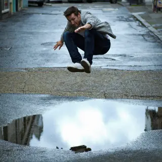 A man captured mid-jump over a puddle, body in the air with 