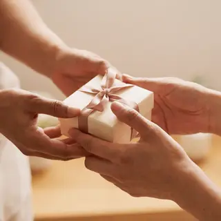 One person handing a small gift box to another person, both 