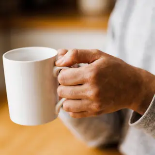 A person holding a white ceramic coffee mug by the handle wi