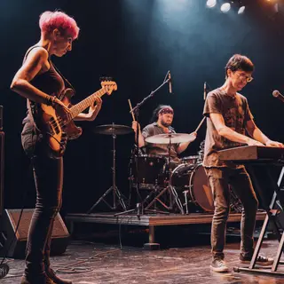 Three musicians on stage: a tall woman with short pink hair 