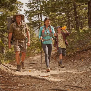 Three hikers on a trail: a man with a backpack and sunhat, a