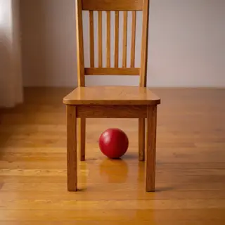 A red ball underneath a wooden chair