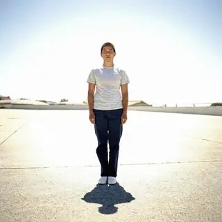 A person standing outdoors at midday with a short shadow dir