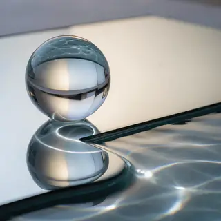 A clear glass sphere sitting on a mirror surface near a pool