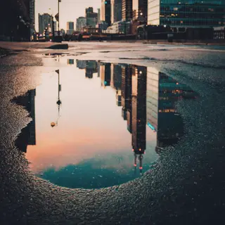 A city skyline reflected in a rain puddle on a street, with 