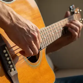 A person playing an acoustic guitar with left hand on the fr