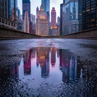 A city skyline reflected in a rain puddle on a street, with 