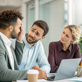 Three coworkers in a meeting: one looking frustrated with fu