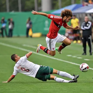 Two soccer players mid-tackle, one sliding and the other jum
