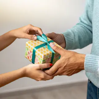 One person handing a small gift box to another person, both 