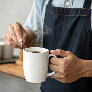 A person holding a white ceramic coffee mug by the handle wi