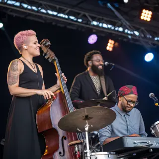 Three musicians on stage: a tall woman with short pink hair 