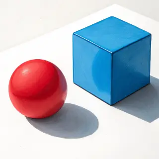 A red ball and a blue cube sitting side by side on a white s
