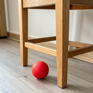 A red ball underneath a wooden chair