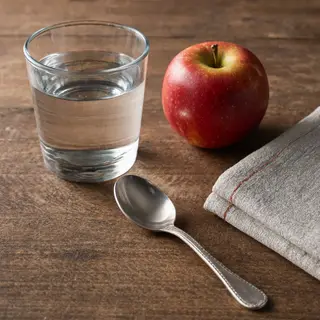 A still life on a wooden table featuring a clear glass of wa