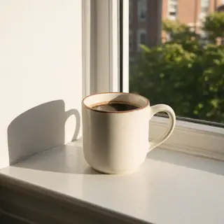 A coffee mug on a sunny windowsill casting a sharp shadow to