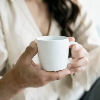 A person holding a white ceramic coffee mug by the handle wi