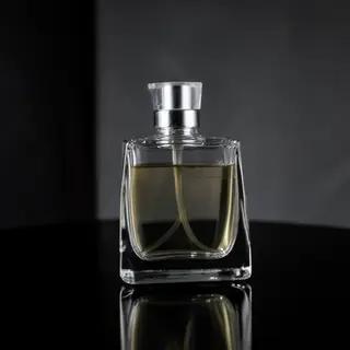 A clear glass perfume bottle on a reflective black surface w