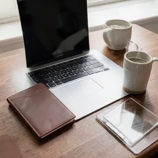 A workspace desk with a brushed aluminum laptop, a leather-b
