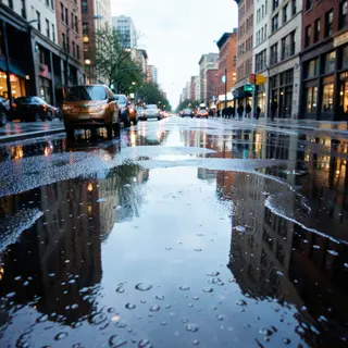 A city skyline reflected in a rain puddle on a street, with 