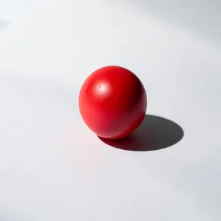 A red sphere on a white surface with a single shadow cast to