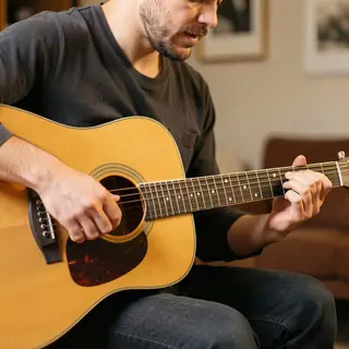 A person playing an acoustic guitar with left hand on the fr