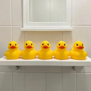 Exactly 5 yellow rubber ducks sitting in a row on a bathroom