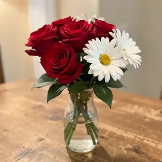 4 red roses and 2 white daisies in a glass vase on a table