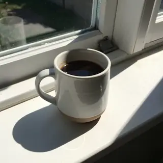 A coffee mug on a sunny windowsill casting a sharp shadow to