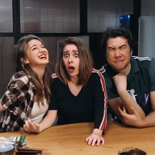 A group of three friends at a table: one laughing with head 