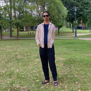 A person standing in a neutral pose in a park, full body vis