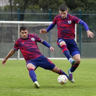Two soccer players mid-tackle, one sliding and the other jum