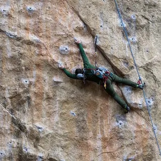 A rock climber clinging to a cliff face with arms and legs e