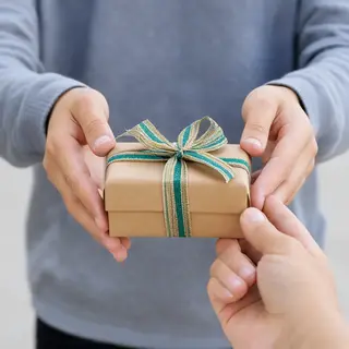 One person handing a small gift box to another person, both 
