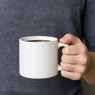 A person holding a white ceramic coffee mug by the handle wi