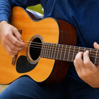 A person playing an acoustic guitar with left hand on the fr