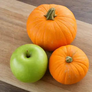A green apple and an orange pumpkin on a wooden cutting boar