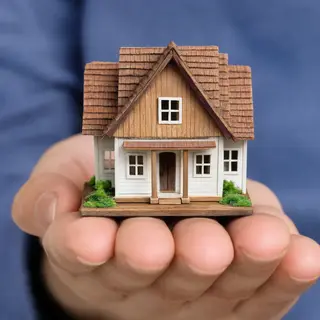 A miniature house sitting on the palm of someone's hand
