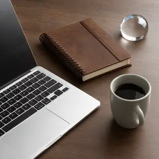 A workspace desk with a brushed aluminum laptop, a leather-b